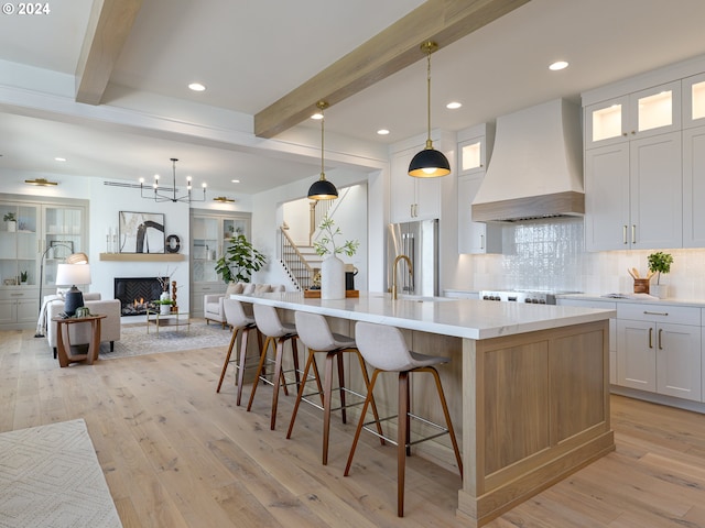 kitchen featuring premium range hood, white cabinetry, beamed ceiling, and a large island