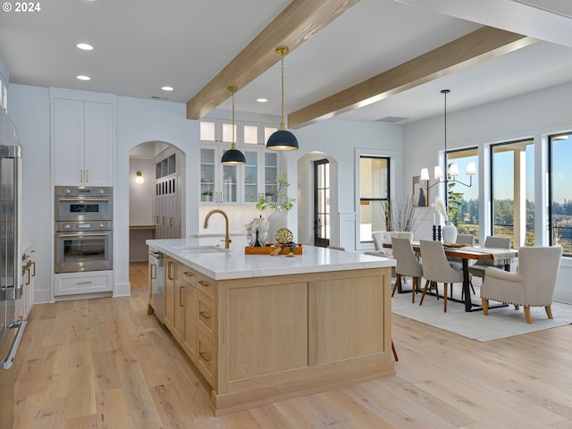 kitchen with double oven, sink, decorative light fixtures, beamed ceiling, and an island with sink