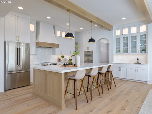 kitchen featuring premium range hood, stainless steel appliances, decorative light fixtures, white cabinets, and a large island