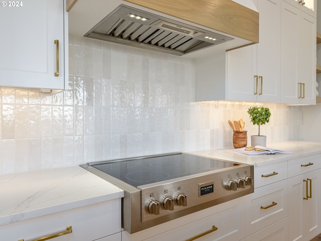 kitchen featuring white cabinets, light stone counters, backsplash, stainless steel cooktop, and custom range hood