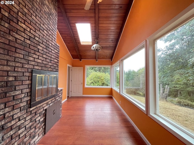 unfurnished sunroom featuring ceiling fan, a brick fireplace, lofted ceiling with skylight, and wooden ceiling