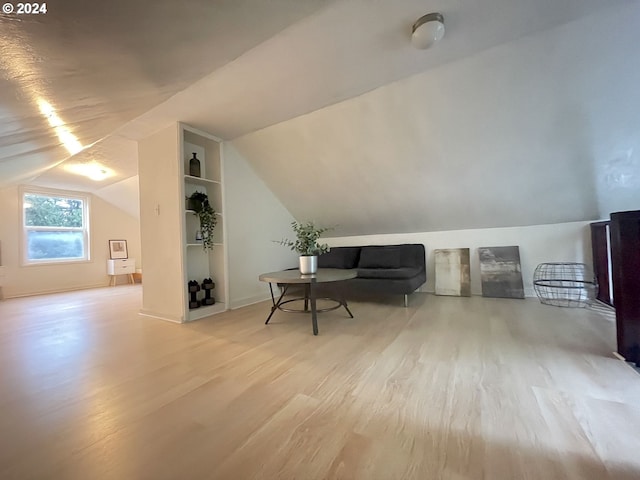 additional living space with light hardwood / wood-style flooring, built in shelves, and lofted ceiling