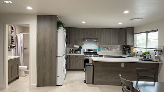 kitchen featuring sink, kitchen peninsula, stainless steel gas stove, backsplash, and stacked washer / dryer