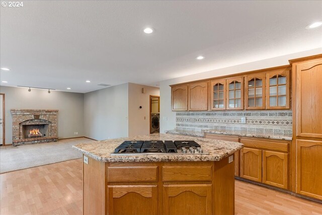 kitchen featuring backsplash, a fireplace, a center island, washer / clothes dryer, and stainless steel gas stovetop