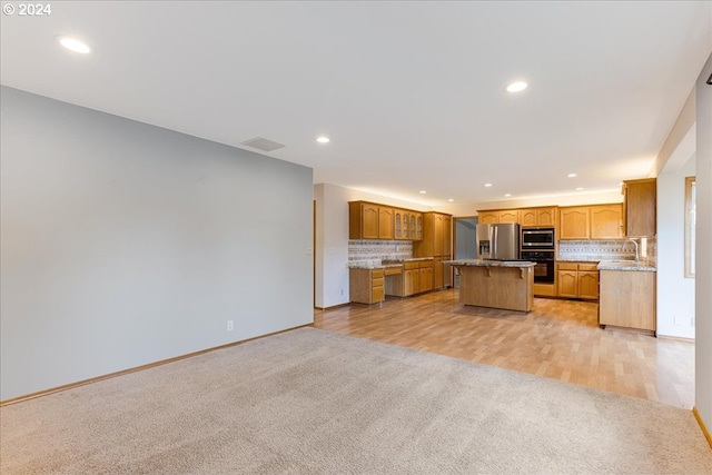 kitchen featuring sink, decorative backsplash, appliances with stainless steel finishes, a kitchen island, and light colored carpet