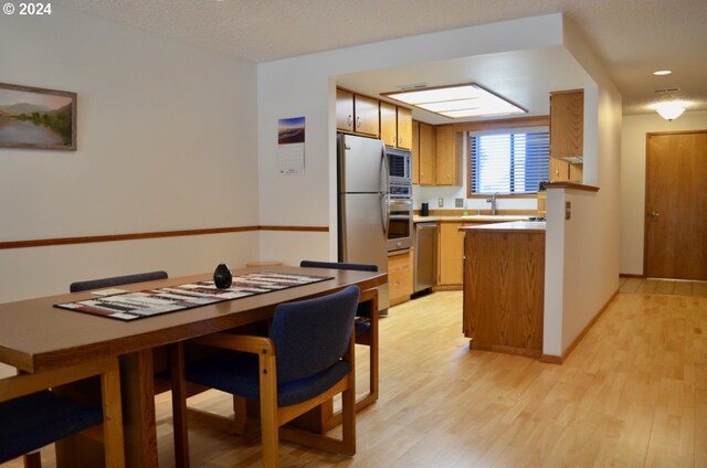 kitchen featuring a textured ceiling, sink, kitchen peninsula, light hardwood / wood-style flooring, and appliances with stainless steel finishes