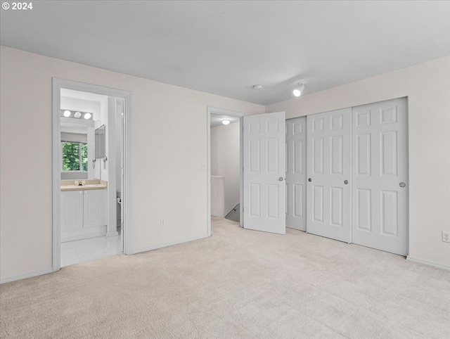 unfurnished bedroom featuring a closet, ensuite bathroom, and light carpet