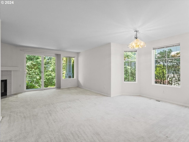 unfurnished living room with a fireplace, a healthy amount of sunlight, light colored carpet, and a notable chandelier