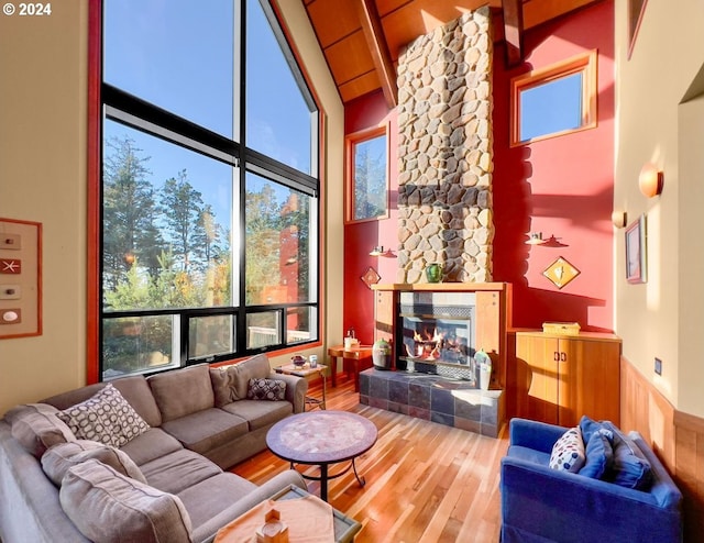 living room with plenty of natural light, a stone fireplace, wood-type flooring, and high vaulted ceiling