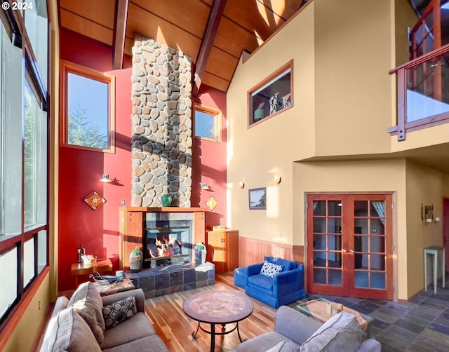 living room featuring french doors, wood ceiling, beam ceiling, high vaulted ceiling, and a stone fireplace