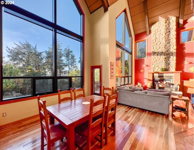 dining space with a stone fireplace, high vaulted ceiling, and hardwood / wood-style flooring