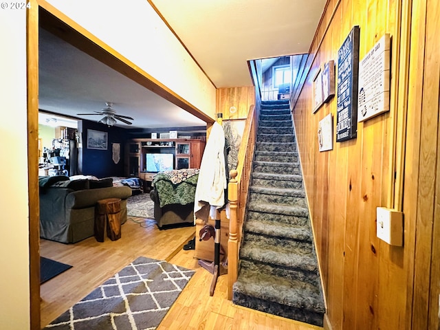 stairway featuring hardwood / wood-style flooring, ceiling fan, and wooden walls