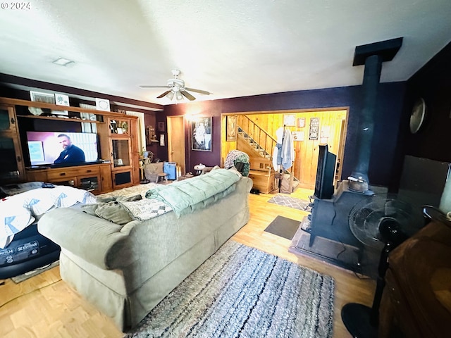 living room featuring ceiling fan, light hardwood / wood-style floors, and a wood stove