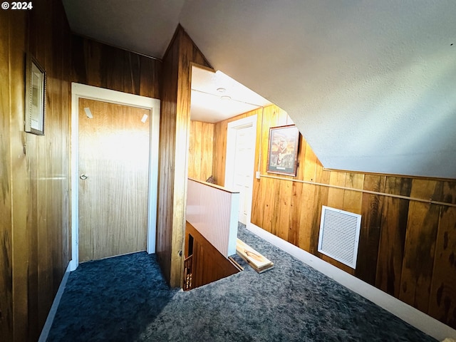 additional living space with dark colored carpet, wooden walls, and vaulted ceiling