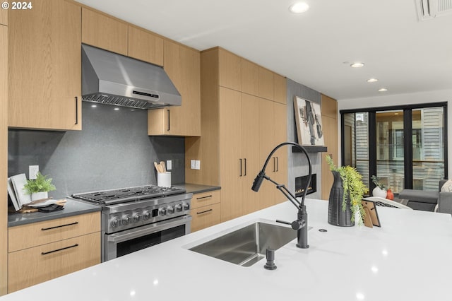 kitchen featuring light brown cabinetry, tasteful backsplash, wall chimney range hood, and stainless steel stove