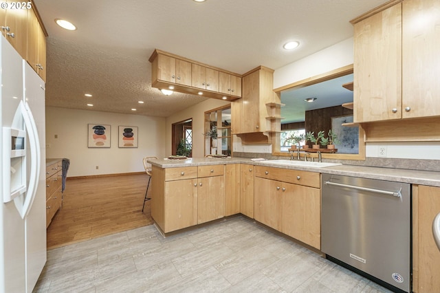 kitchen featuring stainless steel dishwasher, a sink, white fridge with ice dispenser, and light brown cabinetry