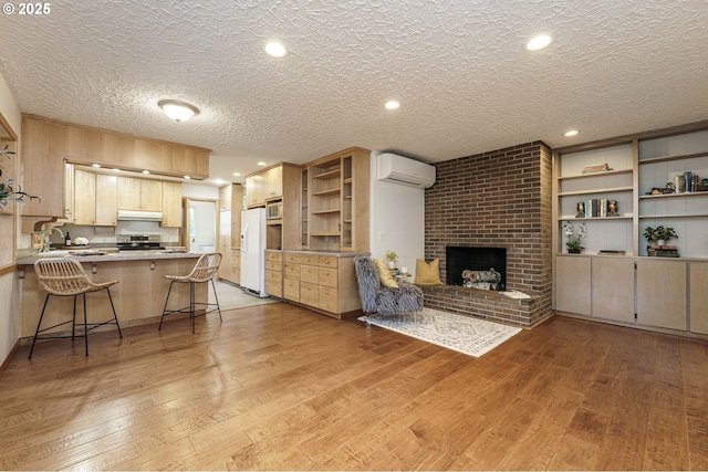 living area featuring light wood-style flooring, a fireplace, a wall mounted air conditioner, and a textured ceiling