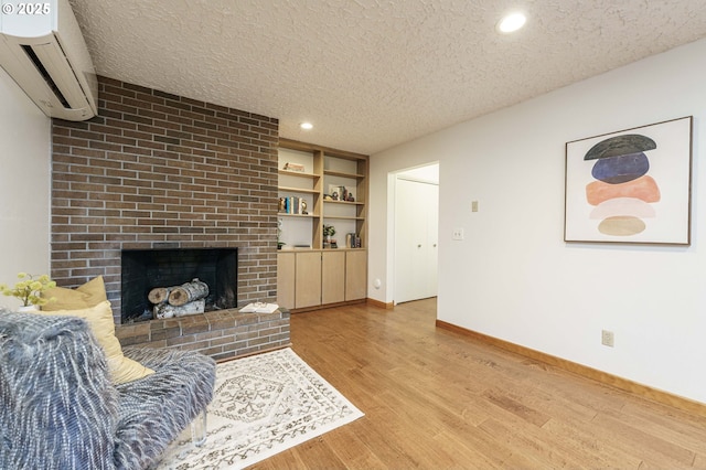 living area with a textured ceiling, wood finished floors, a wall unit AC, baseboards, and a brick fireplace