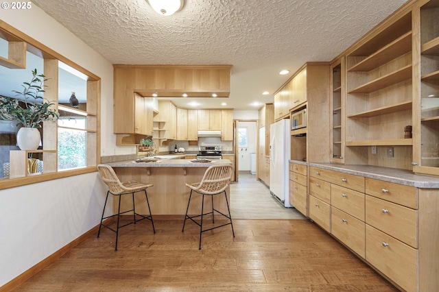 kitchen featuring light brown cabinets, under cabinet range hood, open shelves, white appliances, and a peninsula