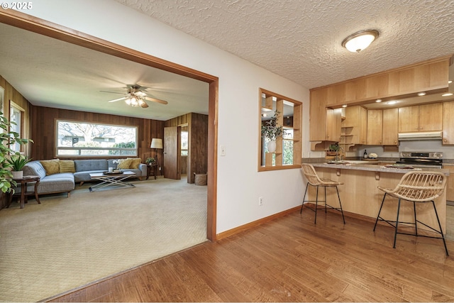 kitchen featuring a breakfast bar area, stainless steel electric stove, light wood-style floors, under cabinet range hood, and open floor plan