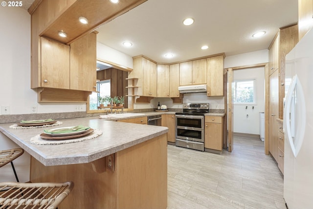 kitchen featuring light brown cabinetry, under cabinet range hood, stainless steel appliances, a peninsula, and light countertops