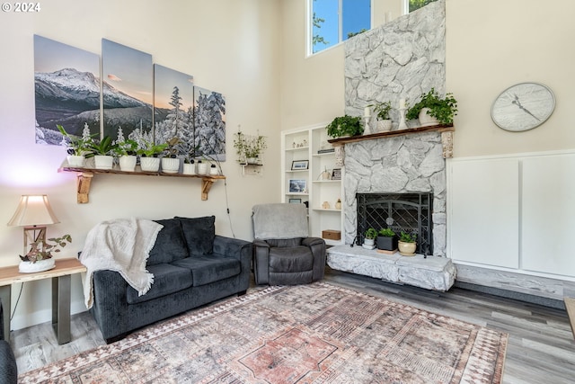 living room with a stone fireplace, a towering ceiling, and wood-type flooring