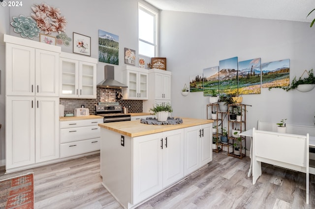 kitchen featuring stainless steel electric range oven, white cabinetry, wall chimney range hood, and butcher block countertops