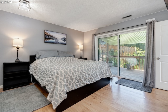 bedroom with access to outside, hardwood / wood-style flooring, and a textured ceiling