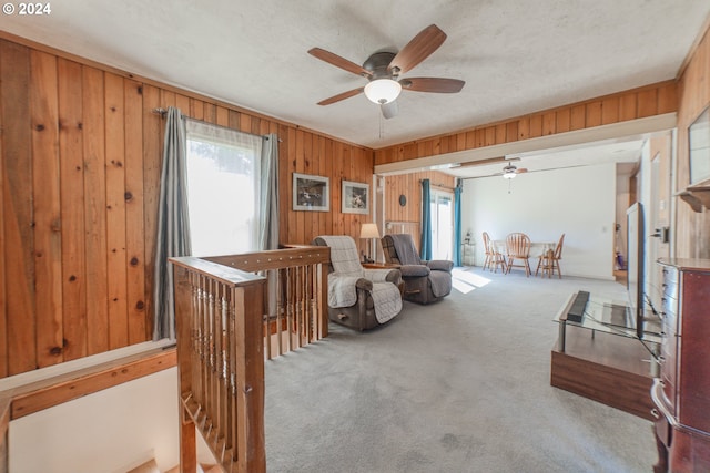 carpeted living room featuring ceiling fan, a textured ceiling, and wooden walls