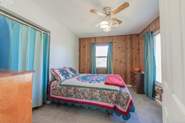 bedroom with ceiling fan, wood walls, and light carpet