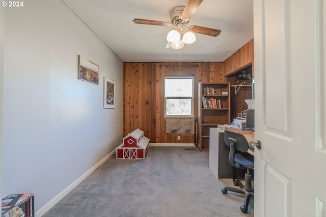 office space with wood walls, ceiling fan, and light colored carpet