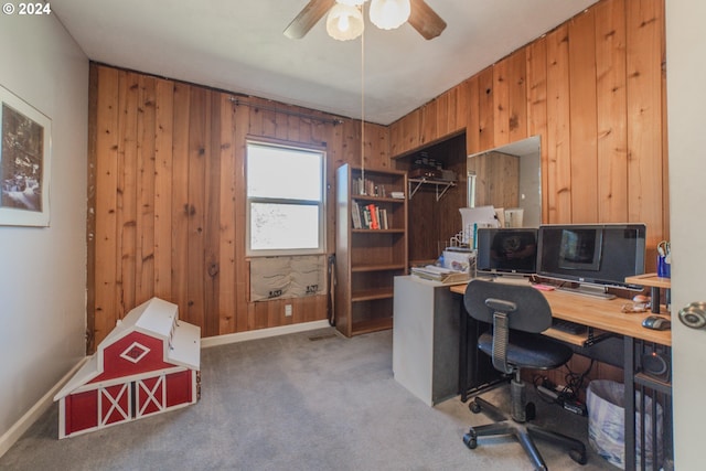 carpeted office featuring ceiling fan and wood walls