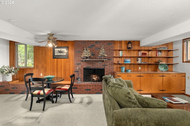 carpeted living room featuring a brick fireplace, a textured ceiling, wooden walls, and ceiling fan