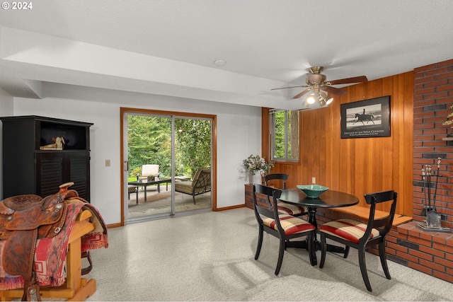 dining area featuring a fireplace, ceiling fan, wood walls, and a textured ceiling