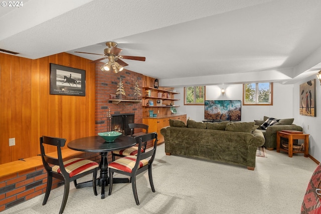 carpeted dining area with a fireplace, a textured ceiling, wooden walls, and ceiling fan