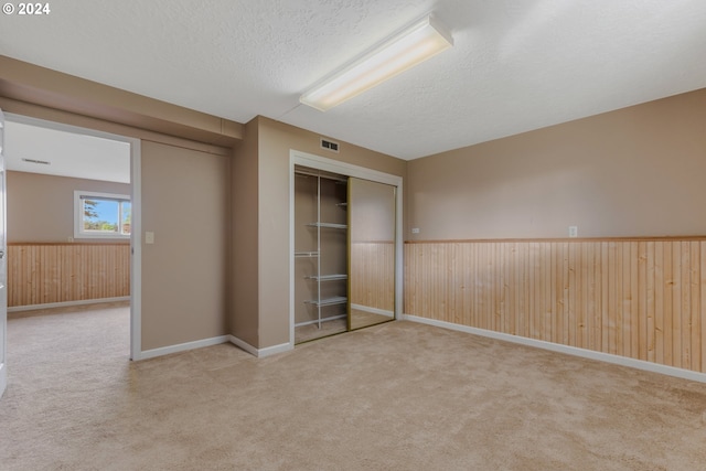 unfurnished bedroom with a closet, a textured ceiling, carpet flooring, and wood walls