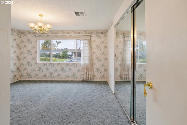 unfurnished room featuring wallpapered walls, visible vents, an inviting chandelier, a textured ceiling, and carpet floors