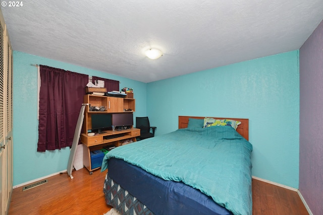 bedroom with a textured ceiling, hardwood / wood-style flooring, and a closet