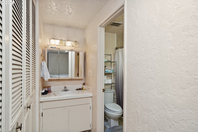 bathroom featuring toilet, a textured ceiling, and vanity