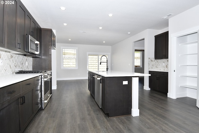 kitchen with a center island with sink, dark hardwood / wood-style flooring, stainless steel appliances, sink, and decorative backsplash