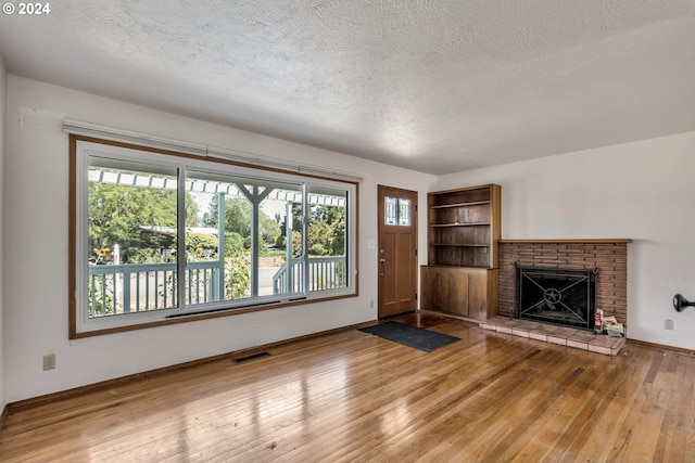 unfurnished living room featuring hardwood / wood-style floors, a textured ceiling, and a brick fireplace