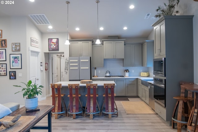 kitchen with gray cabinets, decorative light fixtures, tasteful backsplash, light hardwood / wood-style floors, and stainless steel appliances