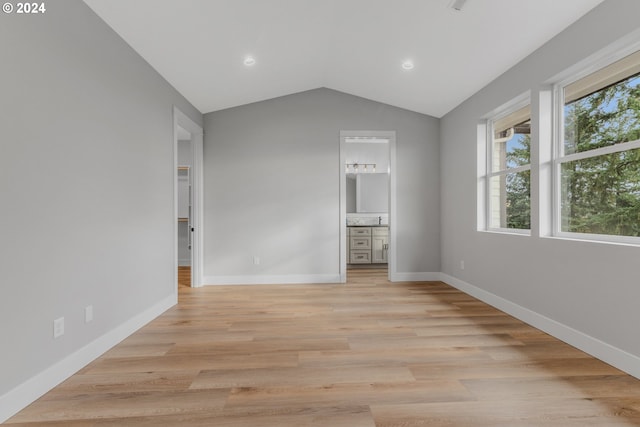 unfurnished bedroom featuring vaulted ceiling, ensuite bathroom, light hardwood / wood-style flooring, and a spacious closet