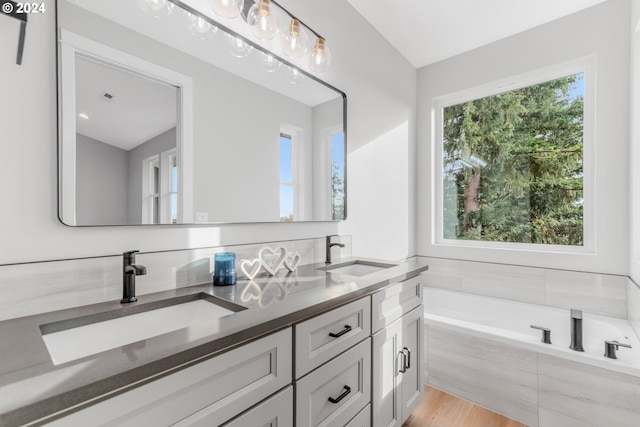 bathroom with vanity, a relaxing tiled tub, a healthy amount of sunlight, and hardwood / wood-style flooring