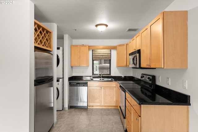 kitchen with light tile floors, light brown cabinetry, sink, stainless steel appliances, and stacked washer / drying machine