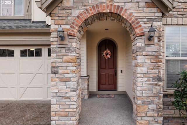 view of exterior entry with stone siding, a garage, and roof with shingles