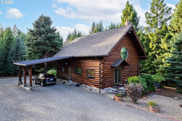 view of front of house featuring gravel driveway, a chimney, a shingled roof, log siding, and a carport