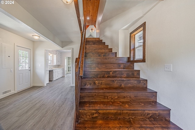 stairway with beamed ceiling, wood-type flooring, and electric panel