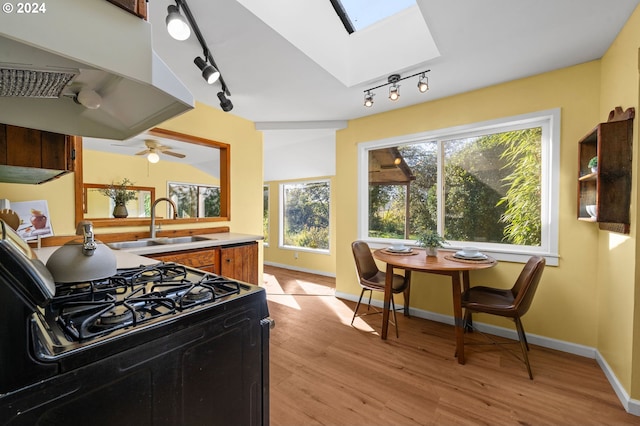 kitchen featuring light hardwood / wood-style floors, a skylight, range with gas cooktop, sink, and track lighting