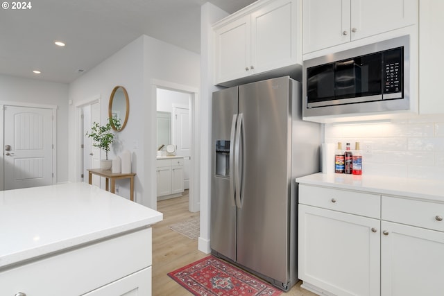 kitchen featuring white cabinets, backsplash, light hardwood / wood-style floors, and stainless steel appliances